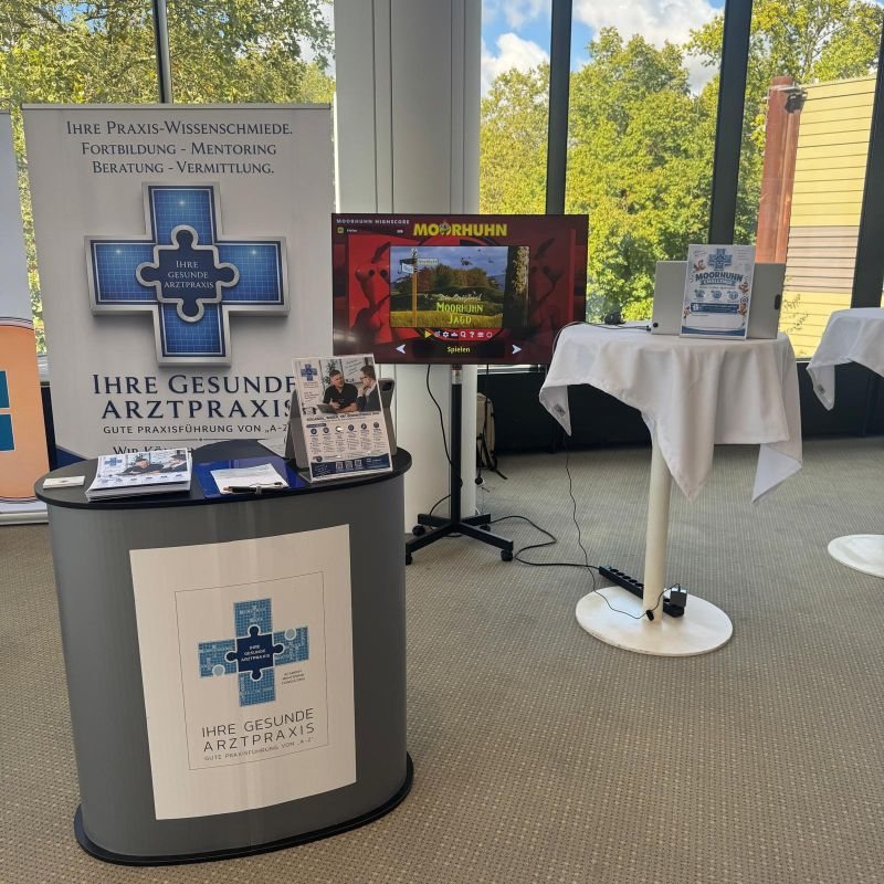 Messestand der Akademie Ihre gesunde Arztpraxis mit MOORHUHN-Spielstation beim DGPRÄC Jahreskongress 2026